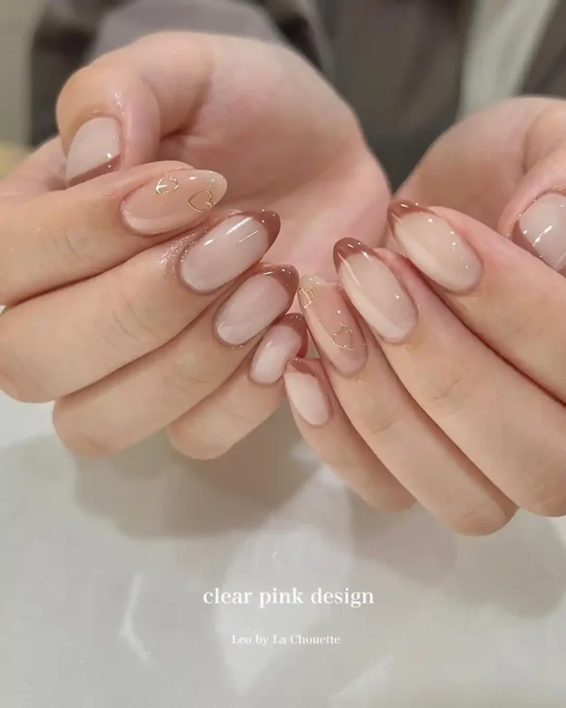 Nude almond nails with chocolate brown French tips and gold chrome hearts. 