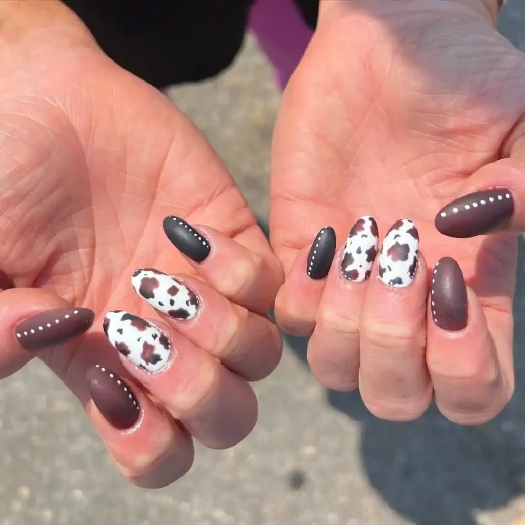 Matte black and brown leather nails with cow print nail art on almond nails.