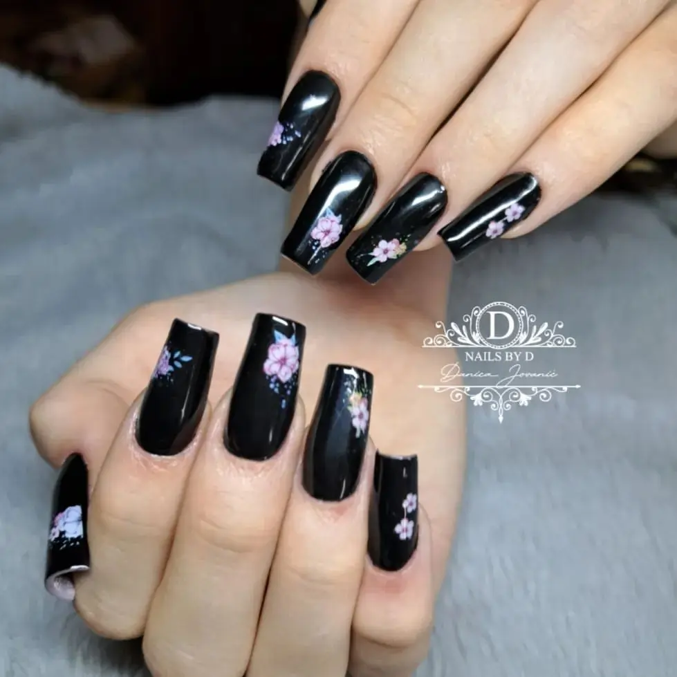 Black square nails with pink floral designs. 