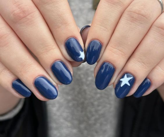 Simple navy blue nails with white star designs. 