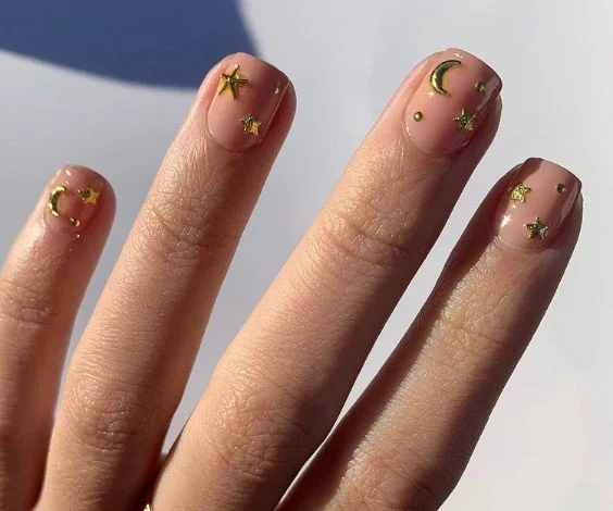 Short nude nails decorated with gold chrome moon and stars.