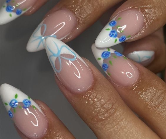 Short almond nails with white French tips and blue flower designs. 