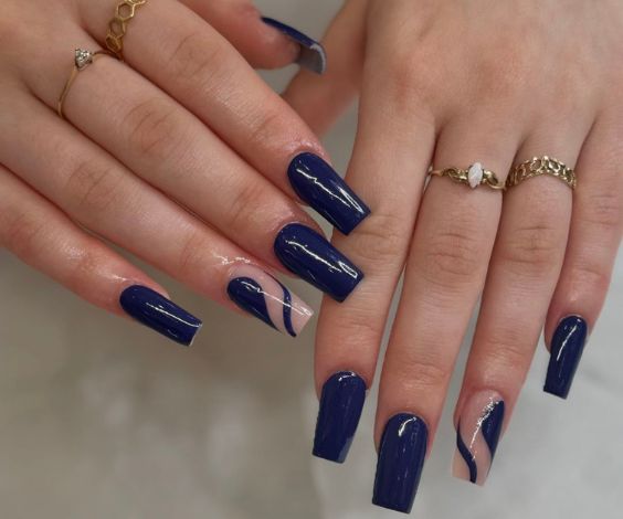 dark blue square nails, featuring nude wavy lines and gold rings on fingers.