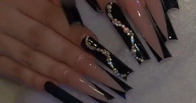 Long black acrylic nails with V tips, glitter nail polish, and rhinestones. 
