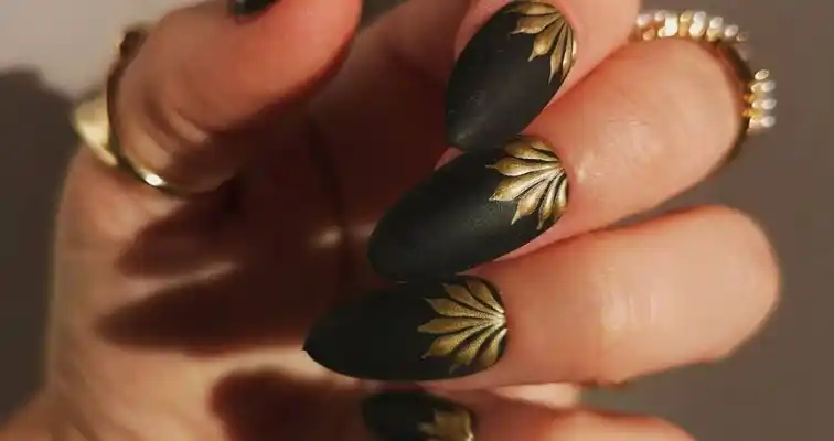 Matte black and gold almond nails with minimal designs. 