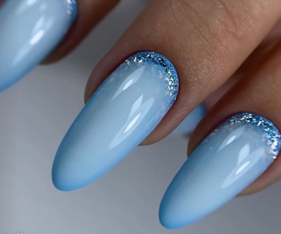 Light blue almond nails with a reverse glitter French manicure.