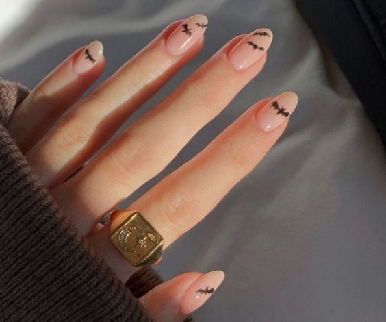 Tiny bat designs on nude oval nails for Halloween. 