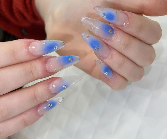 Cute blue aura effect on almond nails with crystal studs.