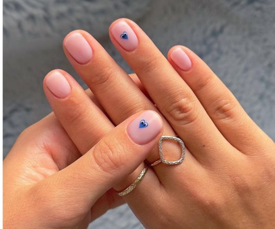 Short nude nails with cute blue heart designs.